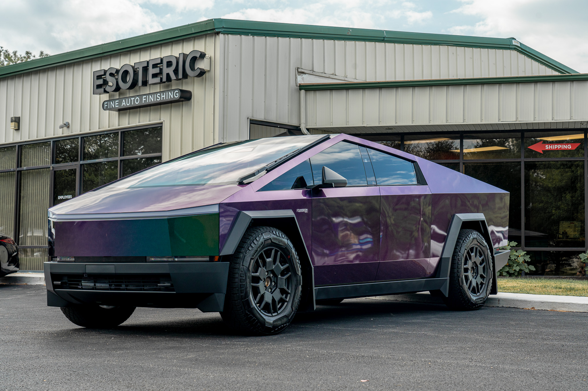 A Rainbow colored Tesla Cybertruck in the Esoteric parking lot on a sunny day, the Esoteric sign is hanging behind the Tesla